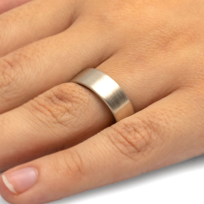May include: A brushed silver wedding band worn on a finger.