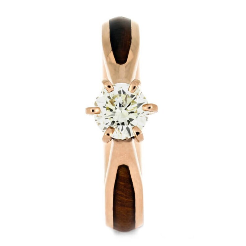 May include: A rose gold engagement ring with a round diamond set in a four-prong setting. The band is made of wood and rose gold.