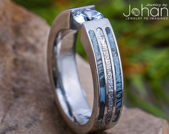 Puede incluir: Un anillo de plata con una piedra preciosa transparente engastada en el centro. La banda está hecha de tres bandas de meteorito azul y plateado.