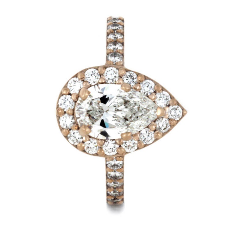May include: A pear-shaped diamond engagement ring with a halo setting. The ring is set in rose gold and features a band of pave diamonds.