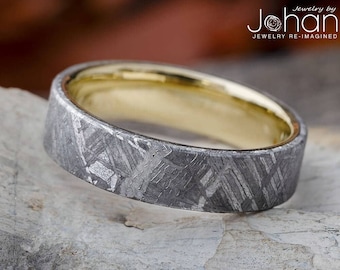 May include: A silver ring with a textured, meteorite-like pattern and a gold inner band. The ring is on a gray, textured surface. Jewelry by Johan. Jewelry Re-Imagined.