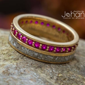 May include: A gold ring with a band of fossilized bone and a row of pink gemstones. The ring is set on a rough, brown rock. The text "jewelry by Johan JEWELRY RE-IMAGINED" is visible in the upper right corner of the image.