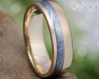 May include: A gold wedding band with a thin band of meteorite inlay. The band is polished and has a smooth finish.  "jewelry by Johan, jewelry re-imagined" is printed on the background.