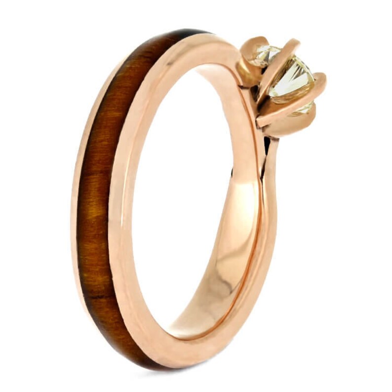 May include: A rose gold engagement ring with a round diamond set in a simple prong setting. The band is made of wood with a tiger's eye inlay.