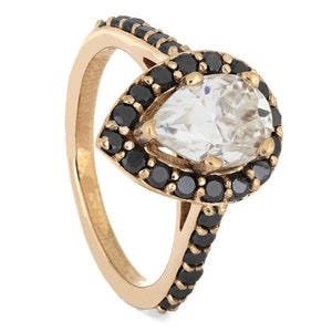 May include: A pear-shaped ring with a large clear stone surrounded by a halo of black stones. The band is gold and has black stones set along the side.