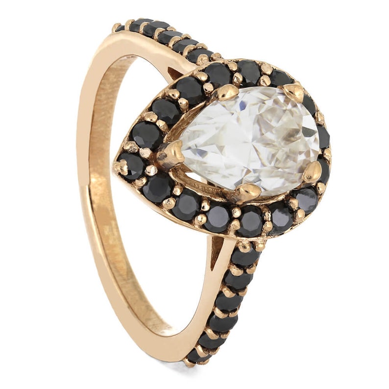 May include: A pear-shaped ring with a large clear stone surrounded by a halo of black stones. The band is gold and has black stones set along the side.