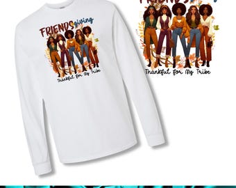 May include: White long-sleeve shirt featuring a graphic of five women in fall attire with the text "Friendsgiving" and "Thankful for My Tribe". The design includes autumn leaves and a color palette of brown, orange, and blue.