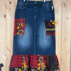 May include: A long denim skirt with a patchwork design. The skirt has a ruffled hem with a floral pattern in shades of red, yellow, and black.