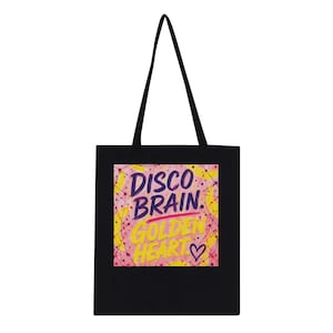 Könnte beinhalten: Eine schwarze Tragetasche mit einem quadratischen Grafikdruck, der den Text DISCO BRAIN in Lila und GOLDEN HEART in Gelb zeigt. Der Hintergrund des Drucks ist ein texturiertes rosa-gelbes Muster mit dünnen Linien und einem kleinen lila Herz.