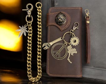 May include: A brown leather wallet with a chain and a variety of keychains attached. The keychains include a peace sign, a wrench, a gear, and a map of Thailand. The wallet has a decorative metal design on the front.