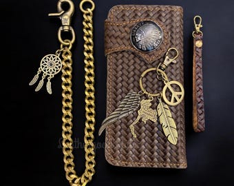 May include: A brown leather wallet with a woven pattern and a metal Native American head design. The wallet has a gold chain attached to it with a peace sign charm, a feather charm, a dreamcatcher charm, and a Thailand charm.