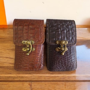 May include: Two leather phone cases with a crocodile pattern. The cases are brown and black and have a brass clasp.