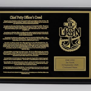 May include: A black plaque with gold lettering and trim. The text reads "Chief Petty Officer's Creed" and includes the USN emblem. A smaller plaque at the bottom displays a name, date, and command name. A commemorative item.