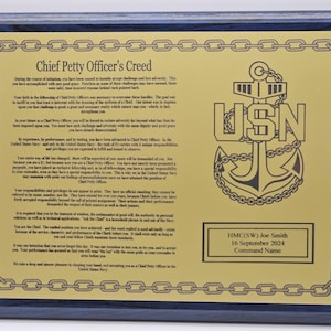 May include: A framed plaque with a gold-colored plate featuring the text "Chief Petty Officer's Creed" and a USN anchor emblem. The plaque has a dark blue wooden frame and a gold chain border. Includes a name, date, and command name.