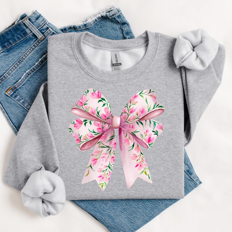 May include: A gray sweatshirt with a pink floral bow design. The bow is made of pink fabric with a floral pattern and is tied in a knot in the center. The sweatshirt is a comfortable and stylish piece of clothing.