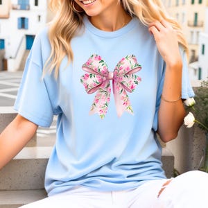 May include: A light blue t-shirt with a pink floral bow design.