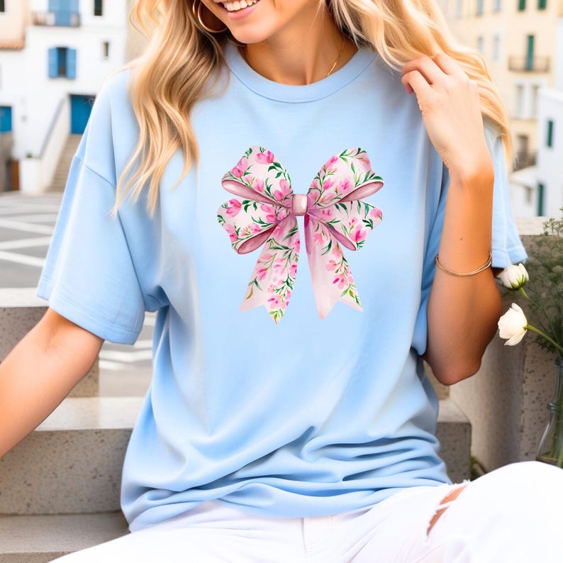 May include: A light blue t-shirt with a pink floral bow design.