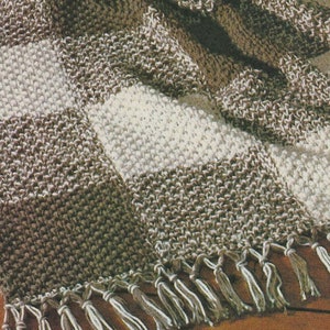 May include: A handmade, checkered blanket in shades of brown and cream, with a fringed edge. The blanket is draped over a wooden floor, showcasing its textured knit pattern. The blanket appears to be approximately 60 inches by 70 inches.