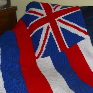 Może przedstawiać: Ręcznie robiony koc z motywem flagi Hawajów. Koc jest w kolorze czerwonym, białym i niebieskim z Union Jack w lewym górnym rogu.