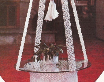 May include: A white macrame hanging plant holder with a glass top, labelled "Glass Slipper" from the book "Macrame Portraits, Book 3, $1.50 by Vickie".
