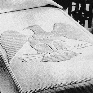 May include: A white crocheted blanket with an eagle design. The blanket is on a bed with a white pillow.