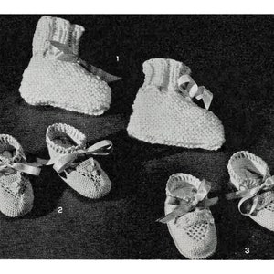 Puede incluir: Cinco pares de botines de bebé tejidos en blanco. Los botines son de diferentes estilos, algunos con un patrón de encaje y otros con un tejido simple. Los botines están atados con cintas blancas.