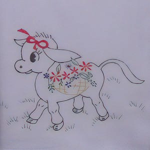 May include: A white embroidered donkey with a red bow, carrying a basket of flowers. The donkey is walking on a field of green grass.