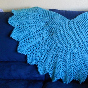 May include: A teal blue crocheted shawl with a scalloped edge. The shawl is draped over a blue couch.