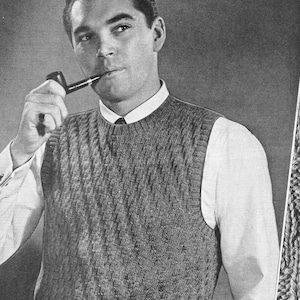 May include: A black and white photo of a man wearing a knitted vest with a cable knit pattern. He is holding a pipe in his right hand and has a serious expression on his face.