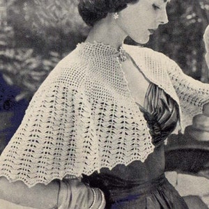 May include: A woman wearing a white crocheted shawl over a black dress. The shawl has a scalloped edge and a delicate lace pattern.