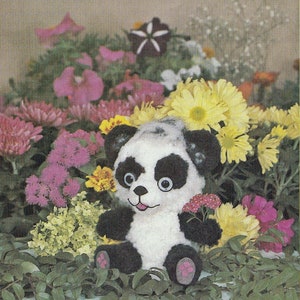 Könnte beinhalten: Ein Plüsch-Panda-Spielzeug in Schwarz und Weiß, das in einem Bett aus bunten Blumen sitzt. Der Panda hat große schwarze Augen und eine rosa Nase.