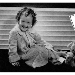 May include: A young girl wearing a knitted coat and skirt set. The coat has a white collar and buttons. The girl is smiling and sitting on a bench.