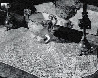 May include: A white crocheted table runner with a delicate floral pattern. The runner is displayed on a wooden table with two decorative glass bowls and a candlestick.