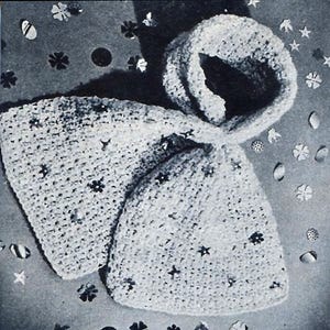 May include: A white crocheted hooded scarf with a star-shaped design. The scarf is laid out on a gray surface with confetti.