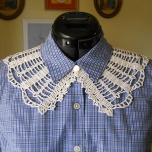 May include: A white crocheted collar with a scalloped edge, worn over a blue plaid shirt.