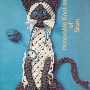 May include: A white and gray crocheted cat with blue eyes and a blue yarn ball. The cat is titled "Honorable Knot-so of Siam".