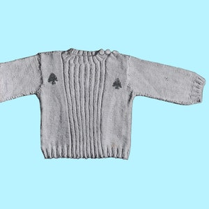 May include: A gray knitted sweater with a crew neck and long sleeves. The sweater has two small tree-shaped designs on the front.