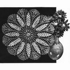 May include: A white crocheted doily with a delicate floral design. The doily is circular and features a central motif surrounded by eight repeating leaf patterns.