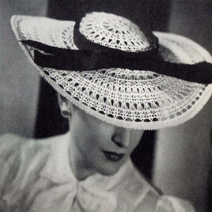 May include: A white crocheted sun hat with a wide brim and a black ribbon around the crown.