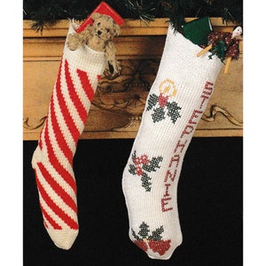 May include: Two knitted Christmas stockings hanging on a wooden mantel. The stocking on the left is red and white striped. The stocking on the right is white with a green holly and red berry design and the text "Merry Christmas" embroidered on it.