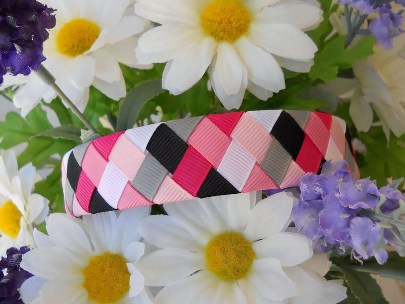 May include: A woven headband with pink, white, black, and gray ribbon. The headband is braided in a diagonal pattern.