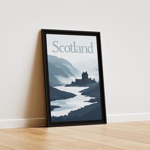 Peut inclure: Impression d'art encadrée représentant un paysage écossais. L'œuvre montre un château au bord d'un lac, entouré de montagnes bleues et grises. Le mot "Scotland" est en haut, en gris clair.