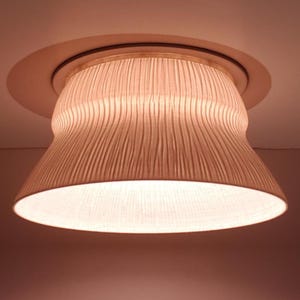 May include: A cream-coloured, textured flush-mount ceiling light. The shade has a distinctive, curved form and a ridged pattern. The light is recessed into the ceiling, with a circular trim around the fixture. The light is approximately 30 cm in diameter.