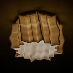 May include: A contemporary ceiling light with a layered, pleated design. The light has a warm, off-white exterior and a bright white interior. The fixture is illuminated, creating a soft glow. The design is geometric.