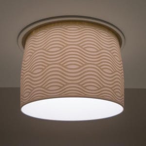 Könnte beinhalten: Eine zylindrische Leuchte mit cremefarbenem Lampenschirm mit einem sich wiederholenden Wellenmuster. Die Leuchte ist an einer weißen Decke montiert und strahlt ein weiches, diffuses Licht aus. Der Schirm hat einen Durchmesser von ca. 20 cm.