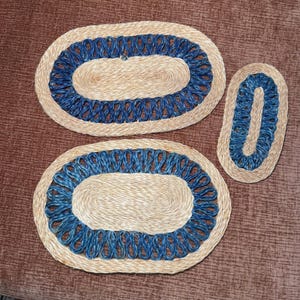 May include: Three oval jute rugs with a blue rope design border. The rugs are in varying sizes, with the largest measuring approximately 30 inches long. The rugs are placed on a brown surface.