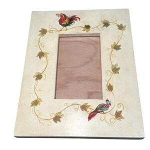 May include: Cream-colored rectangular picture frame with a wooden interior. The frame is decorated with a vine design and two colorful rooster illustrations. The roosters are perched on the vine, adding a rustic charm to the frame.