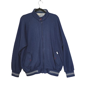 May include: A navy blue zip-up jacket with a stand-up collar and two front pockets. The jacket has white stripes on the cuffs and hem. A small tag is visible on the front.
