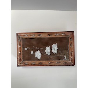 May include: Rectangular wooden framed decorative piece with a brown background. White floral design with a branch and several flowers. The frame is a light brown color with a bamboo-like design.