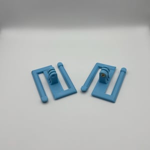 May include: Two light blue plastic camera mounts. Each mount has a rectangular base with a curved top and two vertical supports. A camera attachment is mounted on each base.